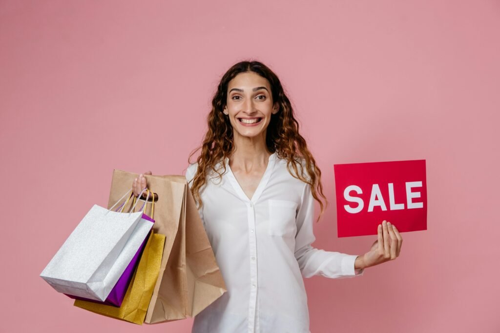 Smiling woman holding shopping bags and sale sign against pink background in studio.
